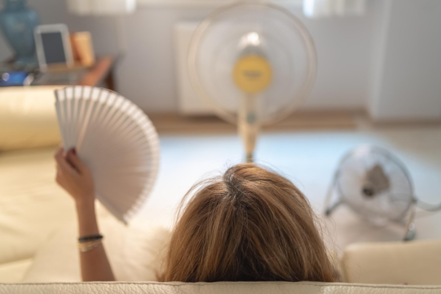menopausal woman sitting on couch with fan blowing on her