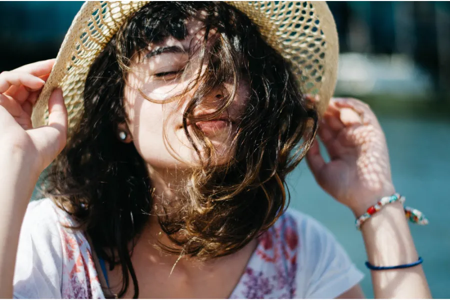 a female holding her hat while enjoying the sunny day with her eyes closed